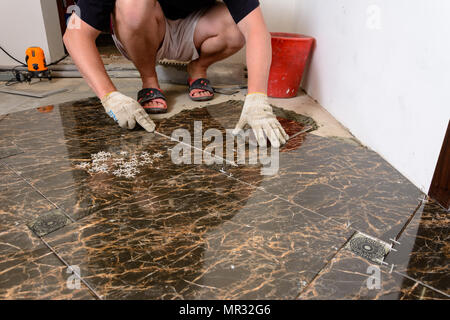 A man places a ceramic tile under pressure over a glue in room of brown color 2018 Stock Photo