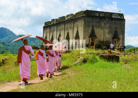Kanchanaburi, Thailand - July 24, 2016: Group of Mon nuns in pink robes holding umbrella walking toward to ruined Buddhist church in Kanchanaburi, Tha Stock Photo