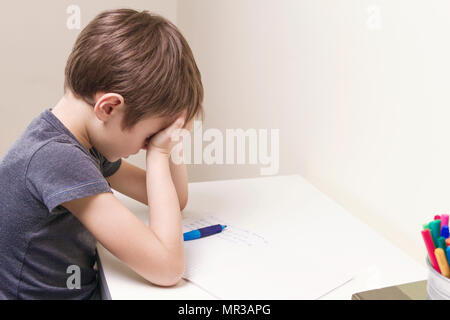 Tired child doing homework at home. The boy fed up and covers his face with hands. Education, school, learning difficulties concept Stock Photo