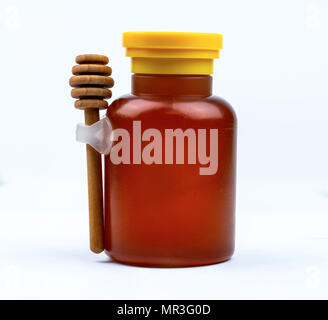 Honey in glass bottle with yellow cap and wooden stick isolated on white background with blank label. Delicious breakfast food concept. Package design Stock Photo