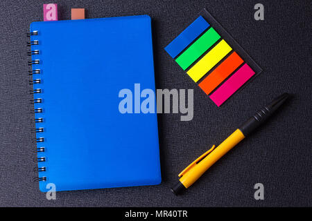 Blue notepad with multi-colored stickers and pen on a black background Stock Photo