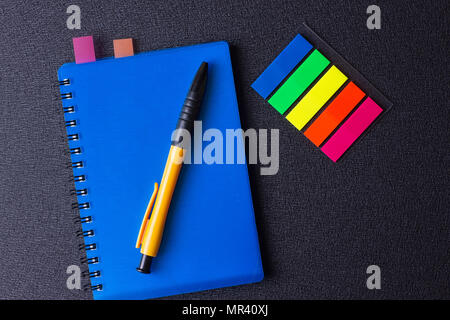 Blue notepad with multi-colored stickers and pen on a black background Stock Photo