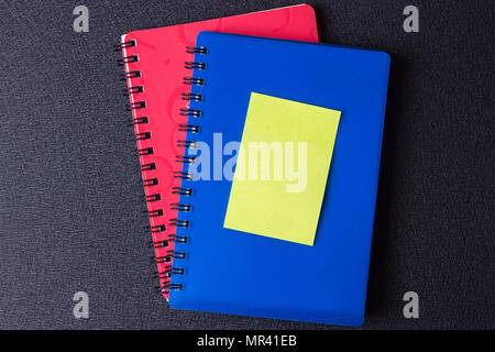 Blue and red notepads on a spiral with a sticker on a black background Stock Photo