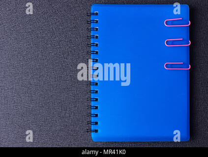 Blue notepad with paper clips on a black background Stock Photo