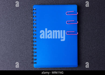 Blue notepad with paper clips on a black background Stock Photo