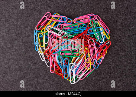 Variety of color paper clips arranged in heart shape on black background. Stock Photo