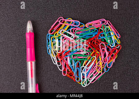 Variety of color paper clips arranged in heart shape on black background. Stock Photo