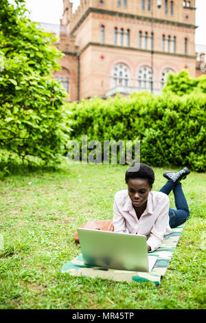 Laughing casual student lying on grass taking notes on campus at college Stock Photo