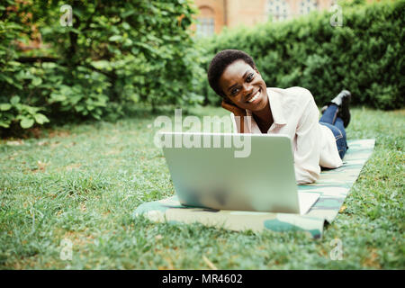 Laughing casual student lying on grass taking notes on campus at college Stock Photo