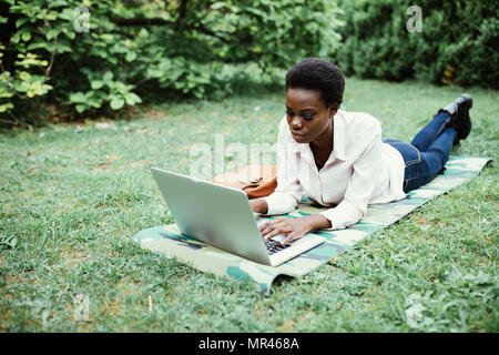 Laughing casual student lying on grass taking notes on campus at college Stock Photo