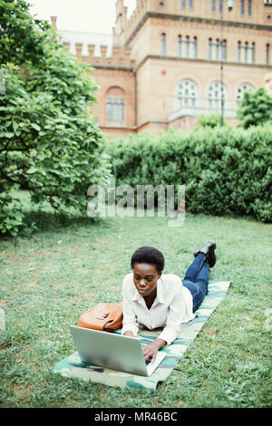 Laughing casual student lying on grass taking notes on campus at college Stock Photo