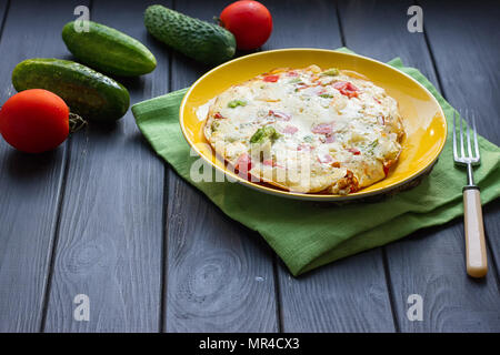 Hearty and tasty breakfast, traditional in the hotel, omelette from chicken eggs with cheese, fresh vegetables - cucumber and tomato on the black wood Stock Photo