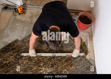 The man checks the surface of the tile using the level 2018 Stock Photo