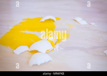 Close up of a broken egg that fell on the floor is splattered with yellow yolk everywhere. Stock Photo