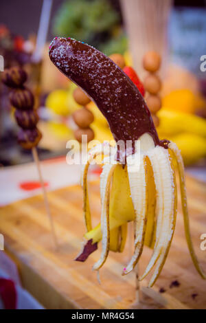 Banana on a stick coated chocolate with coconut chips and colored candies. Stock Photo
