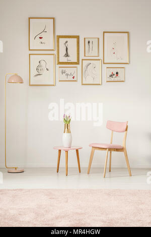 Paintings in golden frames, pink chair, table and lamp set on the white wall in a sitting area interior Stock Photo