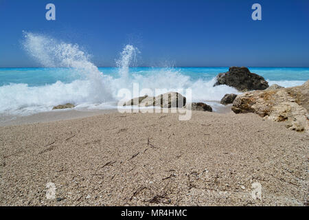 Splashing waves, windy, sunny day, perfect turquoise water, blue sky, rocks and pebble on famous Kathisma beach, Lefkada, Greece Stock Photo