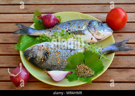 Two raw Sea breams in a plate, soused by salt, olive oil and dry rosemary, ready for grilling, side view Stock Photo