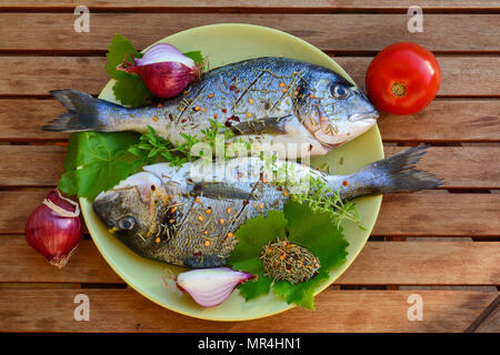 Two raw Sea breams in a plate, soused by salt, olive oil and dry rosemary, ready for grilling, view from above Stock Photo