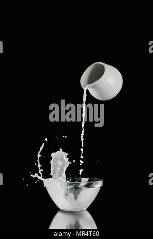 milk pouring from milk jar into bowl on black Stock Photo