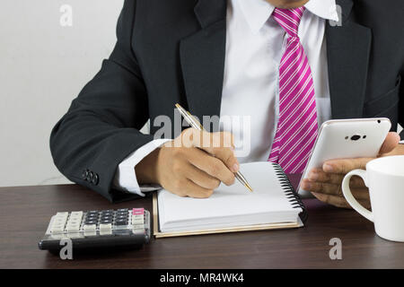 Business man writing on notebook and looking work on phone in work place Stock Photo