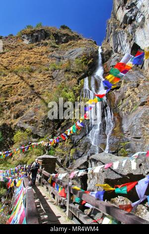 Holy waterfall with colorful Buddhist prayer flags at Taktshang Goemba or Tiger's nest monastery in Paro, Bhutan Stock Photo