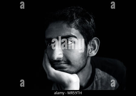 Portrait of a young Asian Indian happily smiling on the results or the joke or a funny tale or story and posing in dark background.Low key portrait. Stock Photo