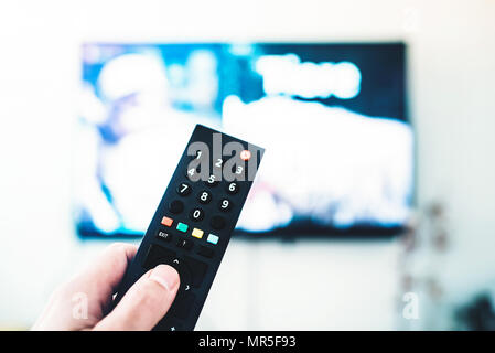person using remote control against TV on white wall Stock Photo