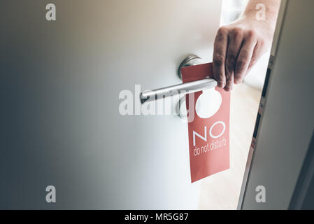 hand placing red do not disturb sign on handle of hotel room door Stock Photo