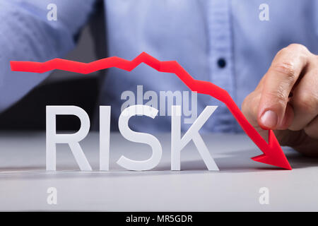 Businessman Pointing Red Diminishing Arrow Over The Risk Text On Reflective Desk Stock Photo