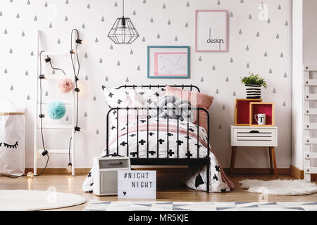 Cute pillows on bed against white wallpaper with grey teardrops in cozy kids room with colorful toys Stock Photo