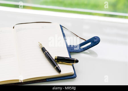 pen and notebook on the white table near window, sideview with green backgrounds Stock Photo