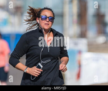 Woman wearing black and sunglasses taking a morning job listening to music on headphones in the UK. Healthy lifestyle. Stock Photo