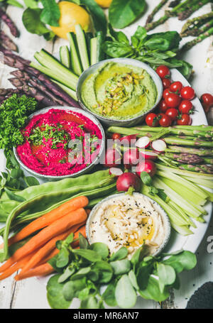 Healthy raw summer vegan snack plate. Chickpea, beetroot, spinach hummus dips with fresh vegetables and greens on white background, close-up. Clean ea Stock Photo