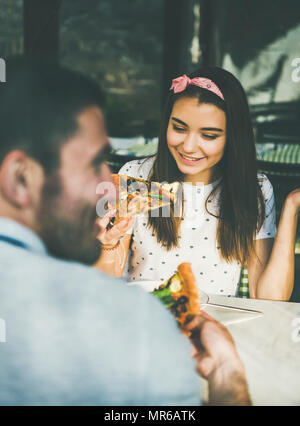 Young happy caucasian couple sitting at table eating pizza in Italian cuisine cafe on sunny summer day Stock Photo