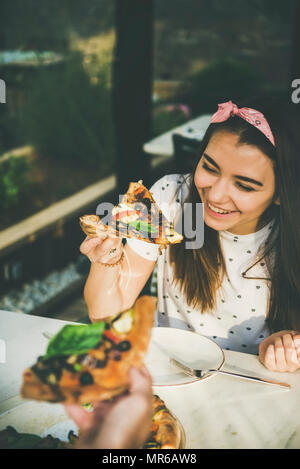 Young happy caucasian couple sitting at table enjoying freshly baked pizza in outdoor Italian cuisine cafe on clear sunny summer day Stock Photo