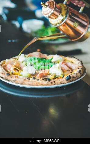 Italian lunch or dinner. Freshly baked pizza with artichokes, smoked turkey ham, olives, cream cheese and basil on table in restaurant, selective focu Stock Photo