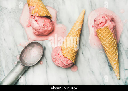 Healthy low calorie summer dessert. Flat-lay of homemade yogurt strawberry ice cream in waffle cones over grey marble background, top view. Dieting, c Stock Photo