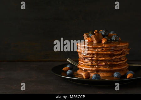 Stack of chocolate pancakes with icing, blueberry, almond, hazelnut and pieces of chocolate. Selective focus. Stock Photo