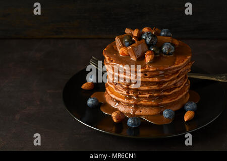 Stack of chocolate pancakes with icing, blueberry, almond, hazelnut and pieces of chocolate. Selective focus. Stock Photo