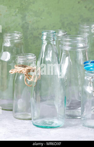 Variety of different shape empty opened glass bottles with and without lids standing on grey table with green wall as background. Stock Photo