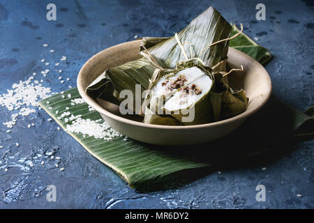 Asian rice piramidal steamed dumplings from rice tapioca flour with meat filling in banana leaves served in ceramic bowlwith rice above over blue text Stock Photo