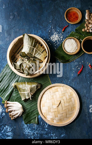 Asian rice piramidal steamed dumplings from rice tapioca flour with meat filling in banana leaves served in bamboo steamer. Ingredients and sauces abo Stock Photo