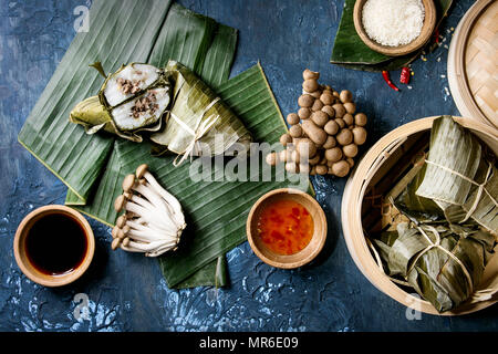 Asian rice piramidal steamed dumplings from rice tapioca flour with meat filling in banana leaves served in bamboo steamer. Ingredients and sauces abo Stock Photo