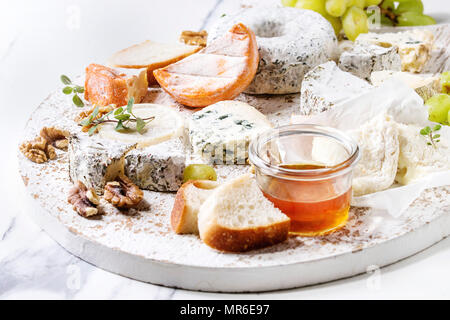 Cheese plate assortment of french cheese served with honey, walnuts, bread and grapes on white wooden serving board over white marble texture backgrou Stock Photo