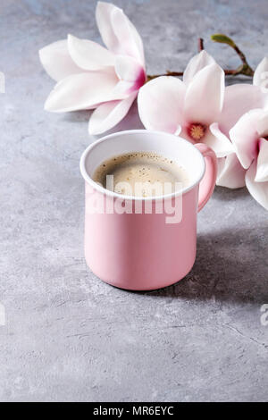 Pink mug of black espresso coffee with spring flowers magnolia branches over grey texture background. Top view, space. Stock Photo