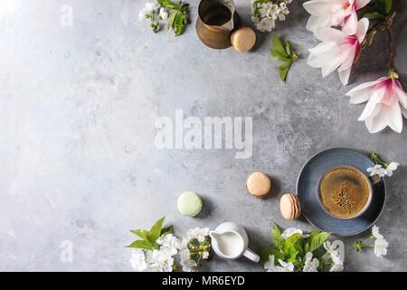 Blue cup of black espresso coffee french dessert macaroons, cream and spring flowers magnolia, blooming cherry branches over grey texture background. Stock Photo