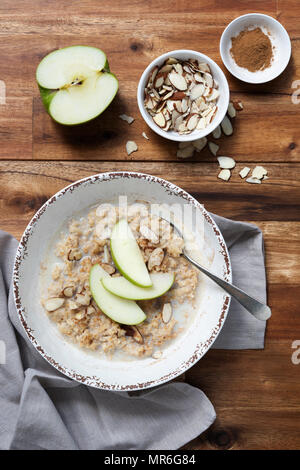 A bowl of traditional oatmeal porridge with sliced apples, flaked almonds and cinnamon on top. Stock Photo