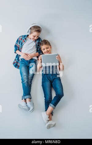 above view of smiling casual kids using digital devices while lying on the floor Stock Photo