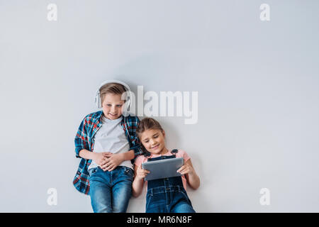 above view of smiling casual kids using digital devices while lying on the floor Stock Photo